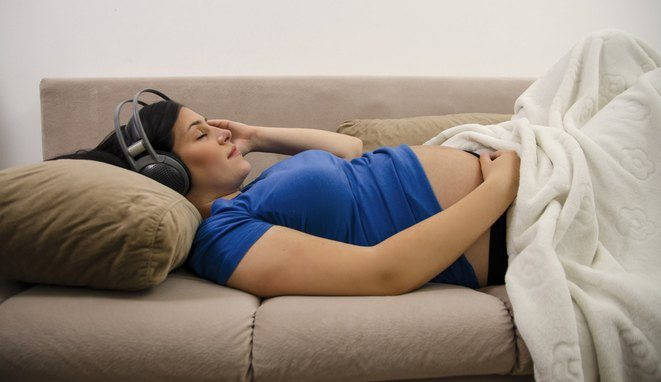 Beautiful Young pregnant woman relaxing listening to music on her comfortable couch