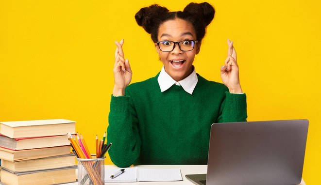 Cheerful black girl crossing fingers, doing homework