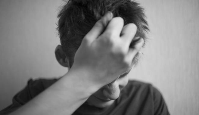 A 18 year old teenager covers his face in despair with his hand