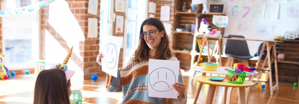 Educación, enseñanza inglés. Una profesora de infantil enseña emociones a una niña.