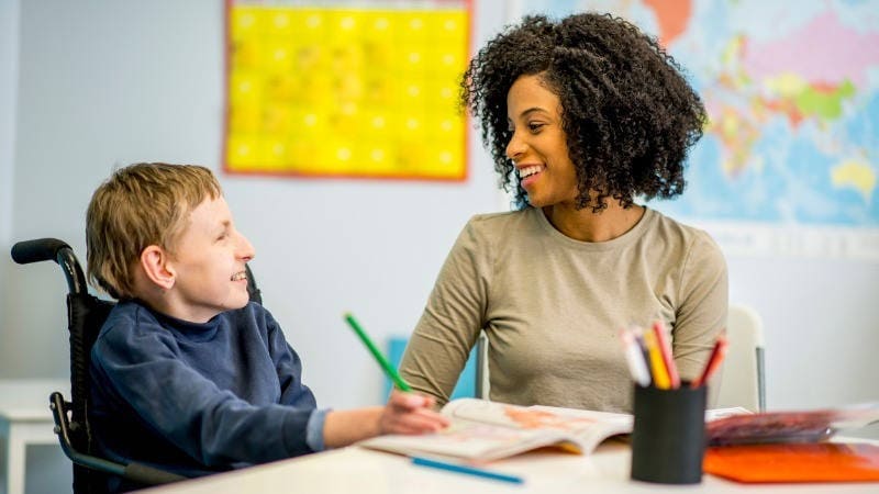 Educación especial, planificación centrada en la persona; un niño con una discapacidad de desarrollo habla y sonríe con su profesora u orientadora