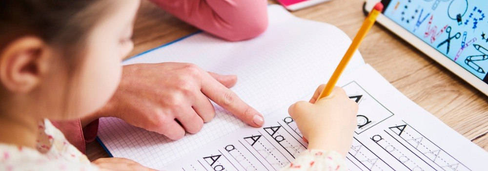 Lectoescritura; una niña practica la escritura del abecedario con su profe.