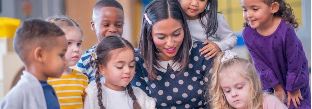 Educación multicultural. Una profesora lee un libro a un grupo diverso de niños de infantil.