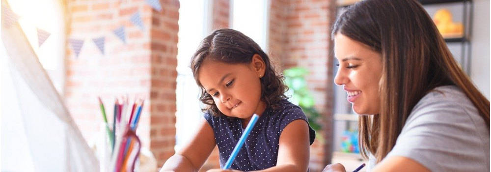 Educación, atención temprana; una profesora sonríe a lado de una niña pequeña dibujando