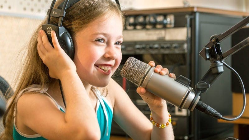 Educación, Enseñanza de la Lengua Inglesa, audio lingual method; una niña sonriente se graba la voz con micrófono y se escucha con cascos