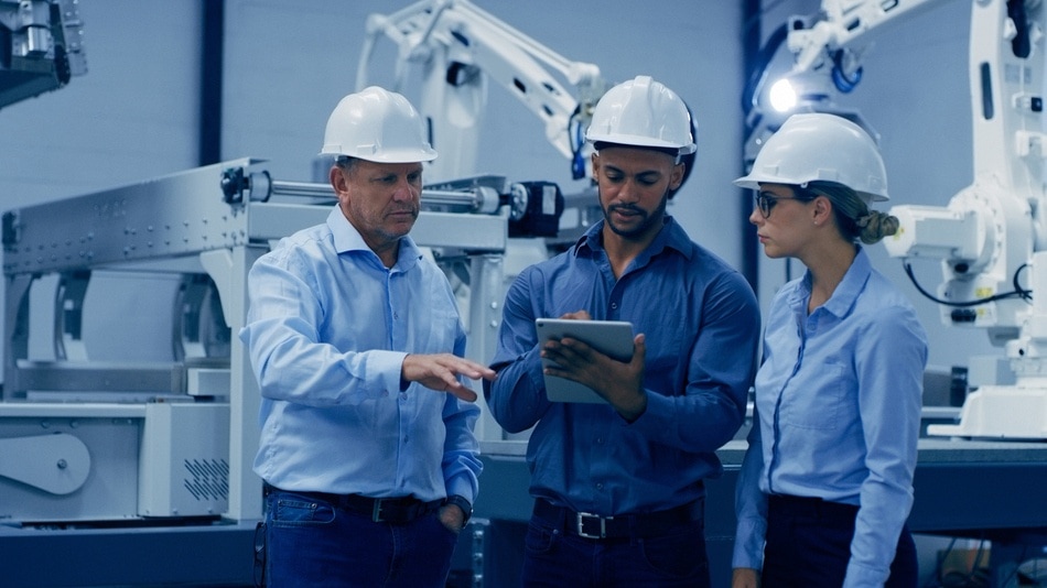 Ingenieros en una fabrica mirando una tablet con brazos de robot a sus espaldas