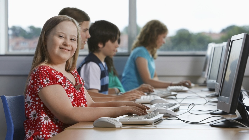 Niña con síndrome de down sonriendo a la camara con sus compañeros utilizando ordenadores