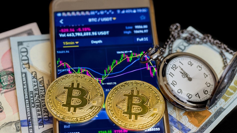 Compra/venta de criptoactivos con un smartphone con dos bitcoins de oro y reloj de bolsillo 