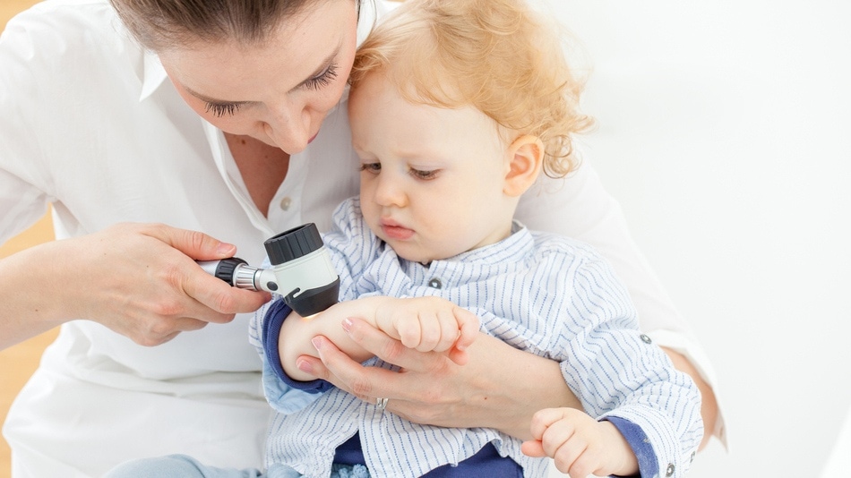 Doctora con un dermatoscopio mirando un lunar en el brazo de un niño