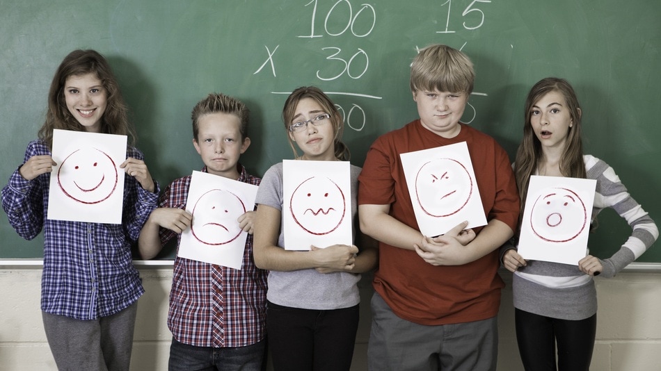 Estudiantes en clase sosteniendo con sus manos un dibujo que representa una emoción
