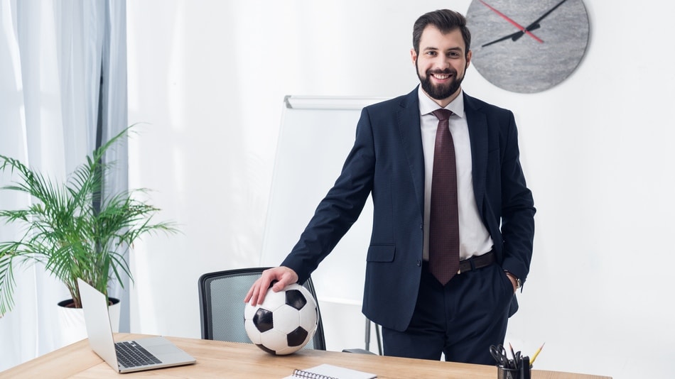 Coordinador deportivo apoya su mano en un balón de fútbol en la mesa de la oficina