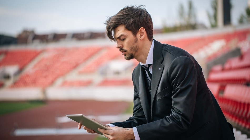 Analista deportivo en la grada de un estadio mirando una tablet