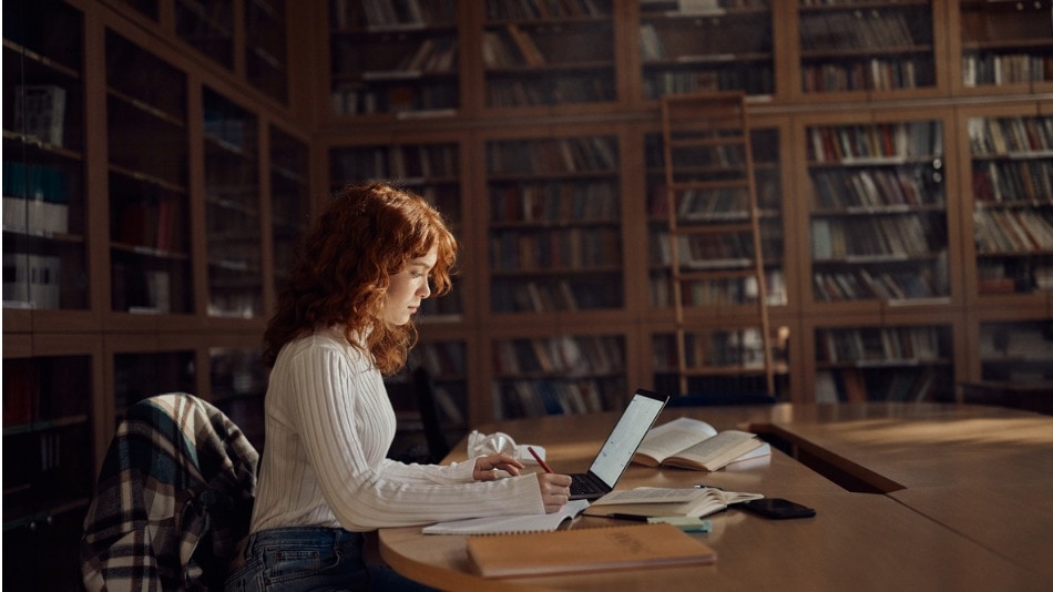 Chica joven tomando notas mientras e-learning en la biblioteca