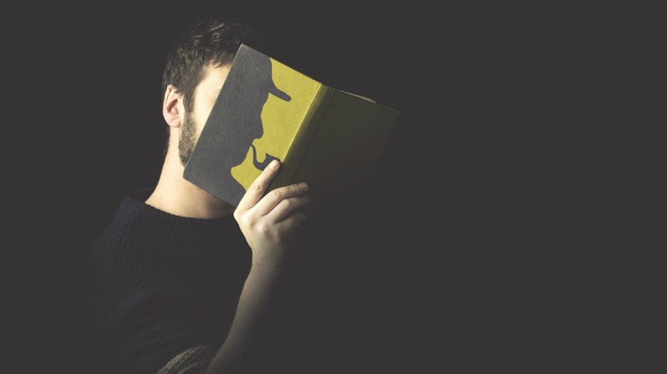 Hombre cubre su cara con en libro abierto en el que aparece la la imagen de un detective