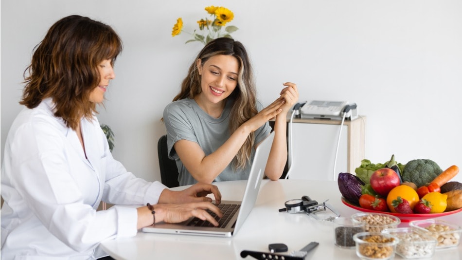 Nutricionista hablando con el paciente en la mesa con computadora portátil