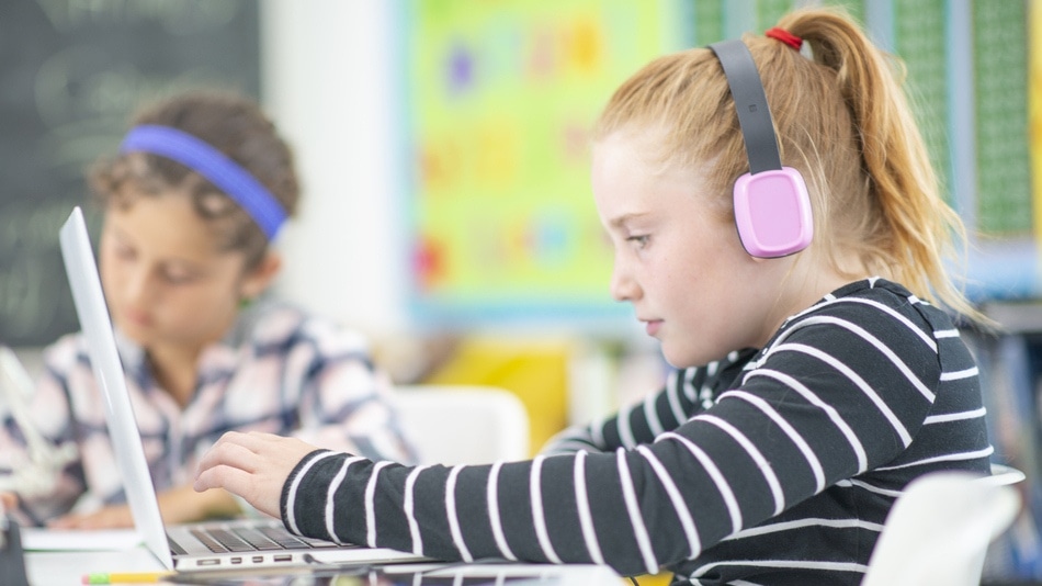 Niña y niño utilizando un portátil y cascos en clase