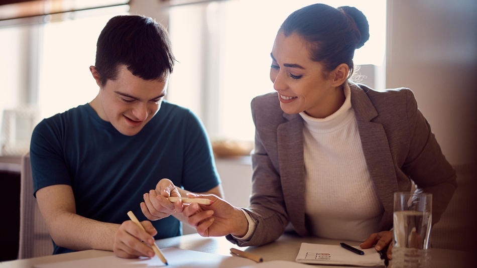 Joven feliz con síndrome de Down que tiene clase de educación especial con su psicólogo en casa