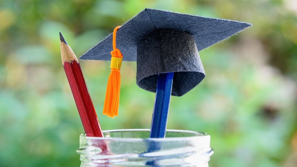 Gorra de graduación negra, lápices azul y rojo en un tarro de cristal