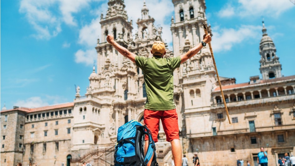 Joven mochilero peregrino de pie con los brazos levantados en la plaza del Obradoiro