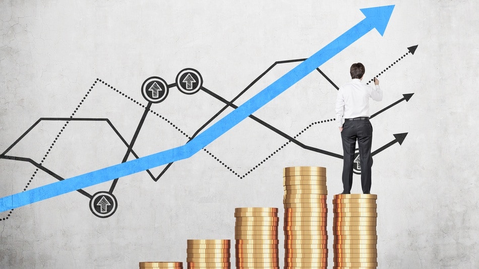 Ejecutivo de espaldas subido a una pila de monedas mirando un gráfico económico