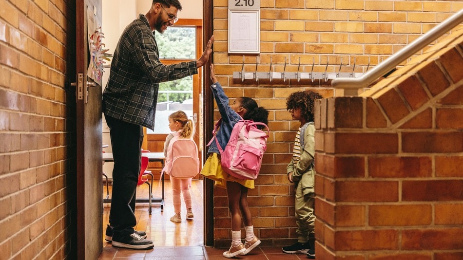 Profesor de educación Infantil saludando a sus alumnos en la puerta de la clase