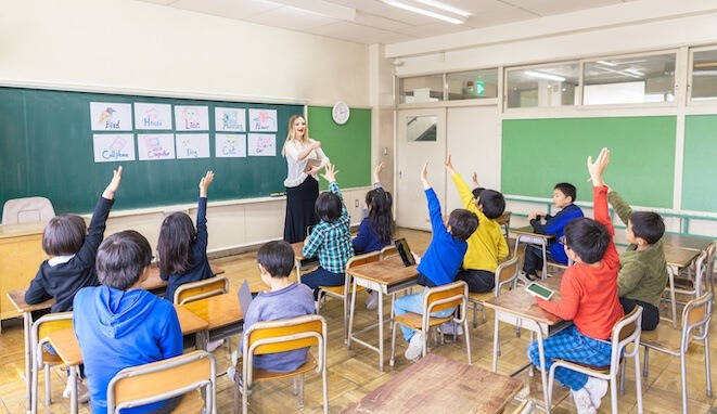 Profesora en clase con niños que levantan la mano. 