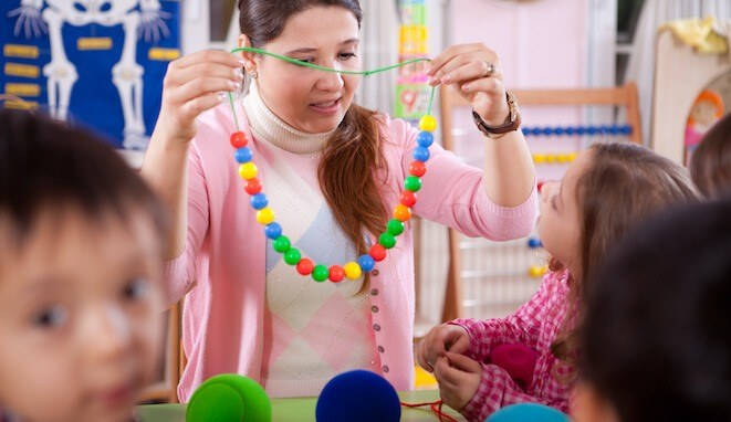 Psicomotricidad fina y gruesa. Profesora enseña un collar de bolas a sus alumnos. 