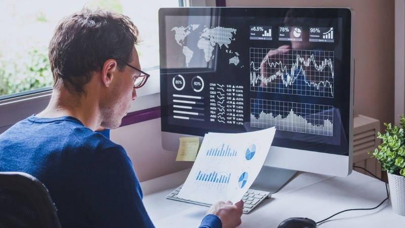 Big Data, bases de datos. Un hombre con gafas viendo gráficos en papel y en el ordenador.