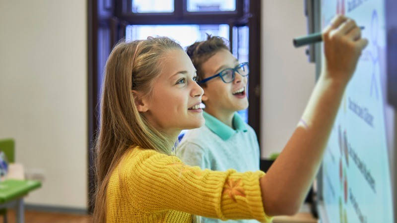 Educación, tecnología, mapa mental. Una niña y un niño escribiendo sobre una pantalla digital interactivo.