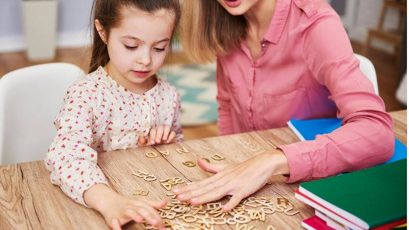 Lectoescritura, abecedario; una niña juega con letras de madera con su profesora para aprenderlas