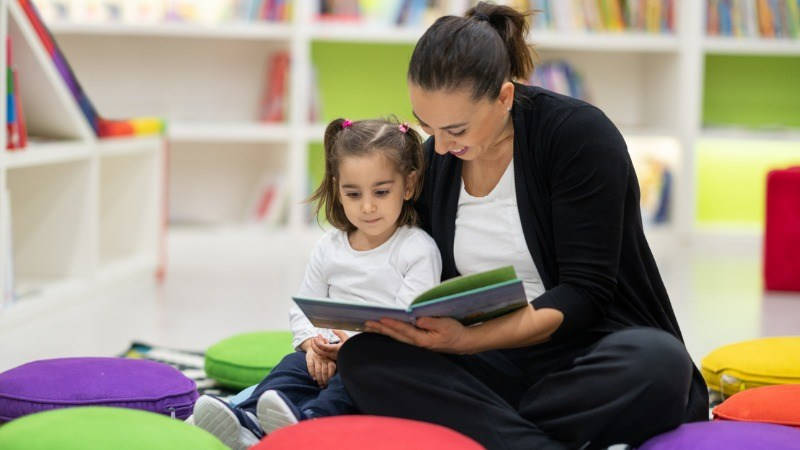 Lectoescritura, lectura, leer; una profesora lee un libro con una niña en infantil