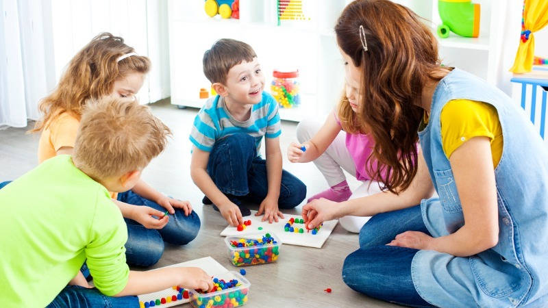 Educación infantil, matemáticas. Niños y profesora clasificando clavijas coloridas.