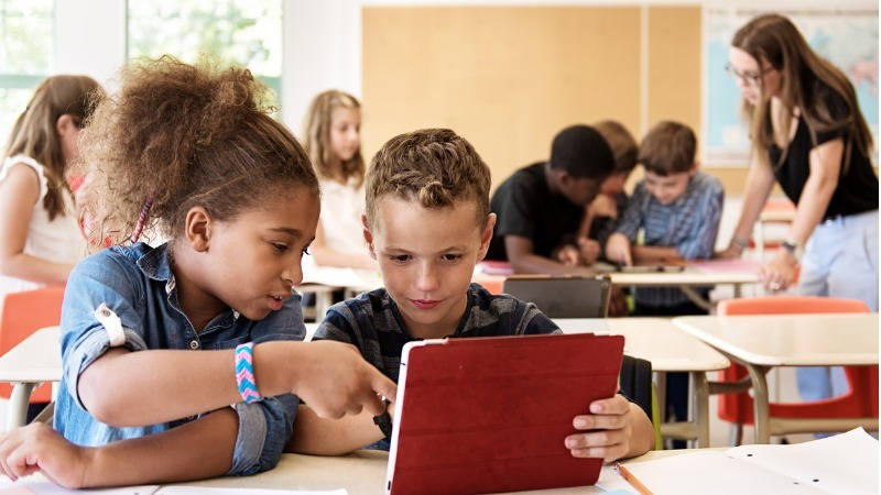 Aprendizaje adaptativo, tecnología; dos niños miran un tablet en la clase, trabajando en grupos.