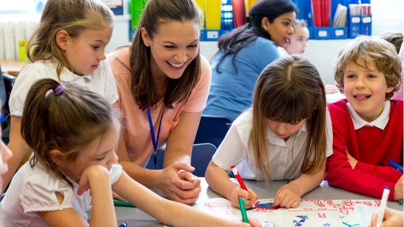 Educación, plástica infantil; un grupo de niños pinta en la misma hoja y la profesora joven sonríe
