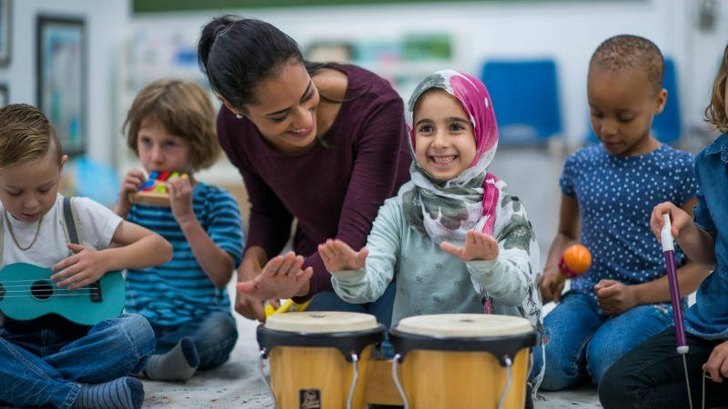Educación inclusiva, ocio inclusivo, inclusión en el aula; una niña con hiyab toca tambores en una clase de música con sus compañeros y la profesora