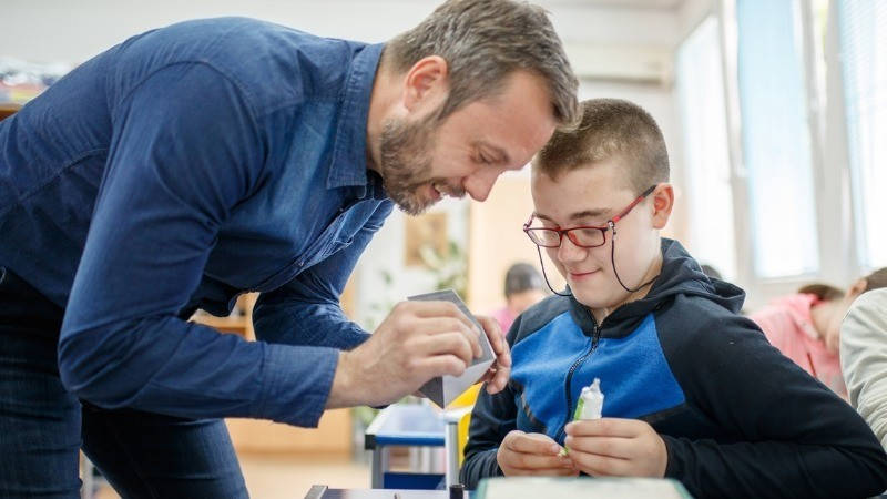 Educación especial; un profesor ayuda a un niño montar una figurita con cola