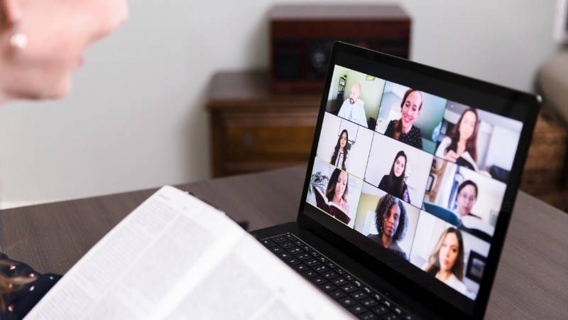 Educación universitaria; una profesora con un libro da clase online, se ven varios alumnos en la pantalla del portátil 