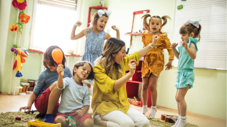 Aprendizaje musical; una profesora en el suelo con niños tocando instrumentos y bailando