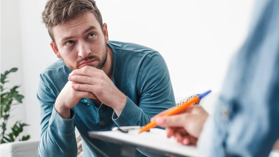 Psicoterapia; un hombre ansioso mira a su terapeuta mientras evalúa en un papel