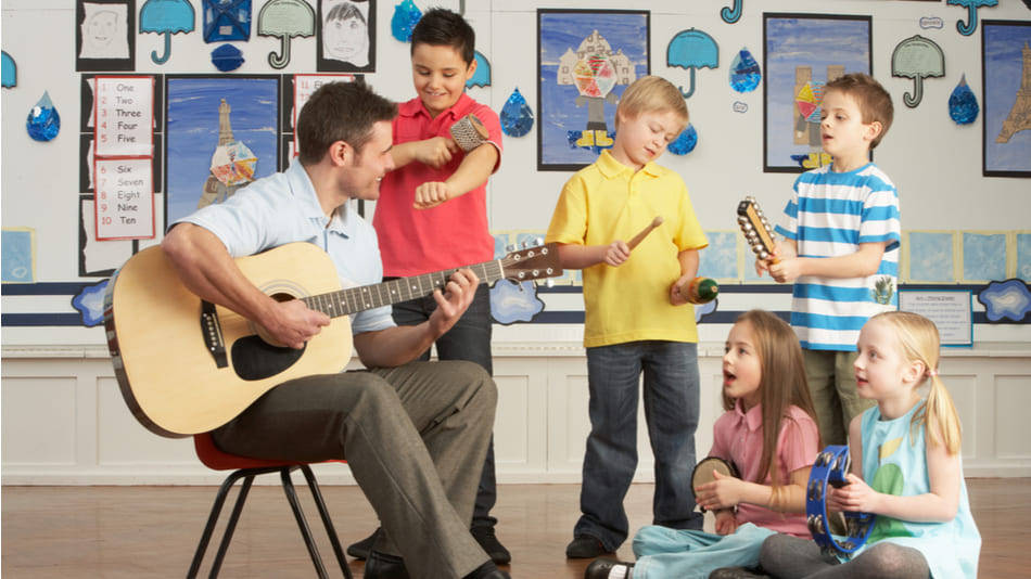 Pedagogía musical, un profe toca guitarra con un grupo de niños con instrumentos