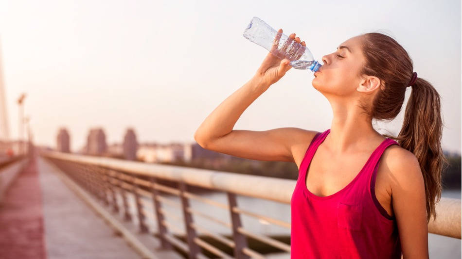 hidratación y deporte; una mujer joven bebiendo agua por la calle