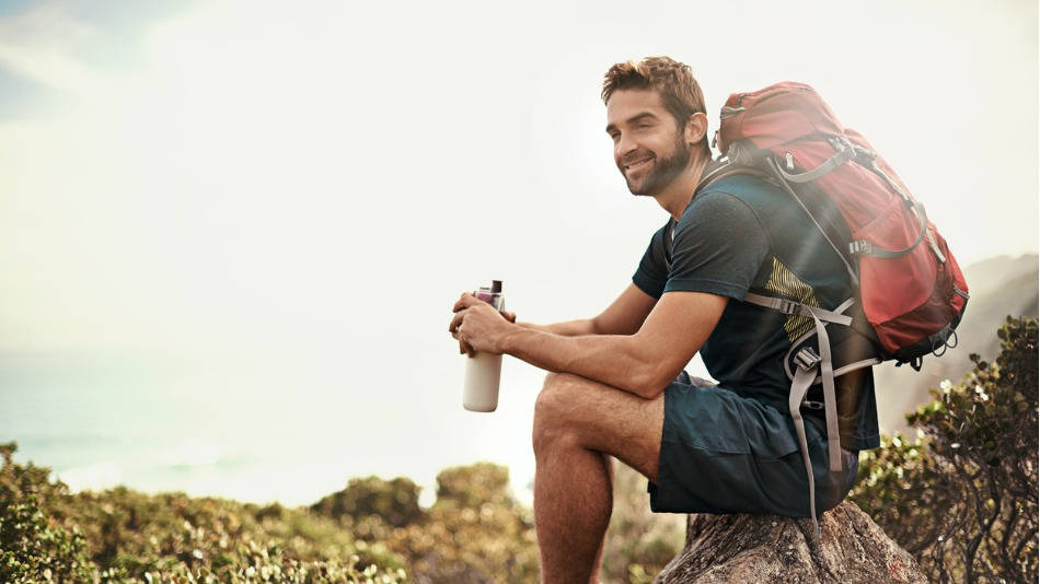 Hidratación en el deporte; un hombre sonriente con mochila descansa para beber agua durante el senderismo