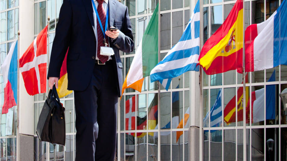 Un hombre en traje camina delante de un edificio con banderas de varios países, bander de España