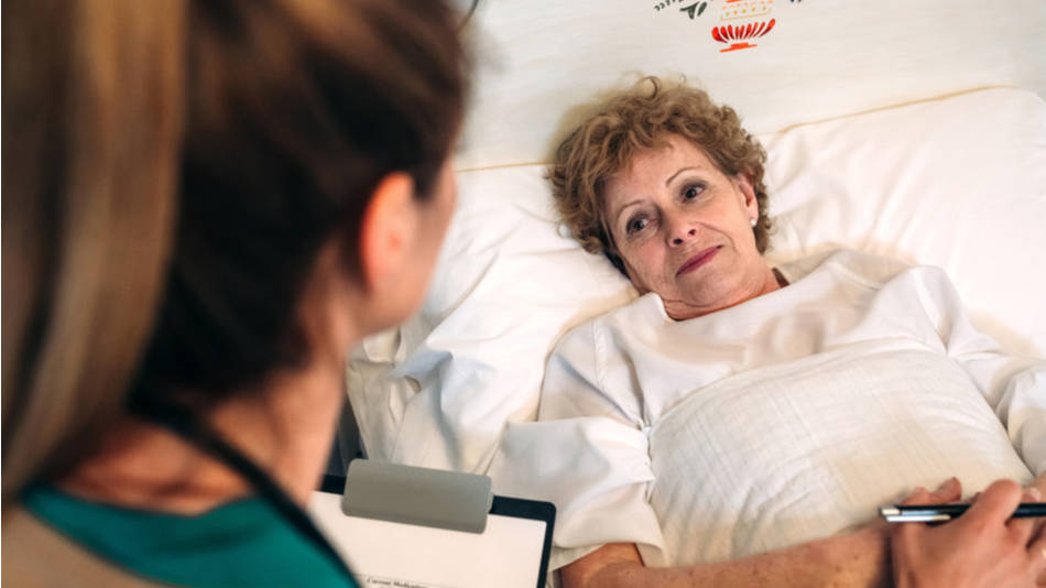 Enfermera con papeles y bolígrafo habla con una paciente mayor tumbada