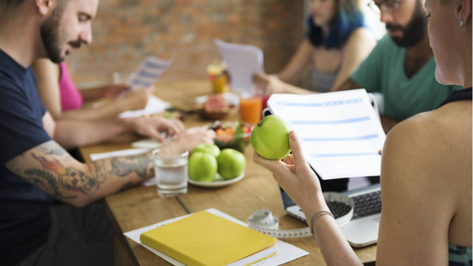 gente reunida en una mesa con informes y frutas